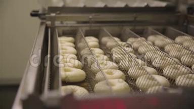 在一个小镇的甜甜圈面包店制作甜甜圈的程序-甜甜圈在油炸锅里油炸。 场景。 准备过程
